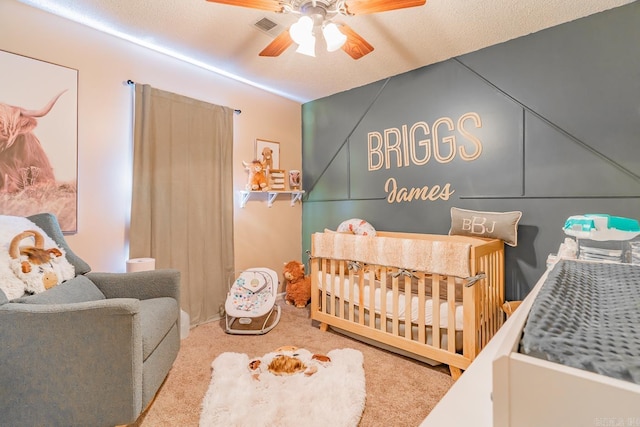 carpeted bedroom with a nursery area, visible vents, ceiling fan, and a textured ceiling