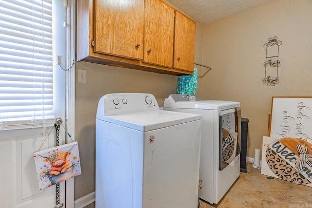 clothes washing area with baseboards, cabinet space, a textured ceiling, and washing machine and clothes dryer