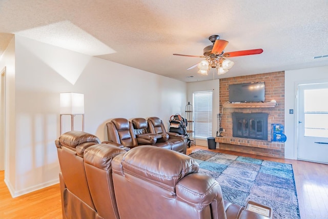 living area with light wood finished floors, ceiling fan, a brick fireplace, and a textured ceiling