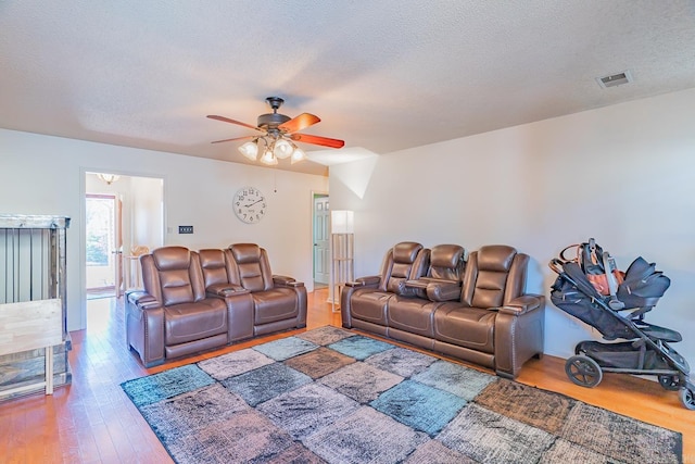 living area featuring a textured ceiling, ceiling fan, wood finished floors, and visible vents