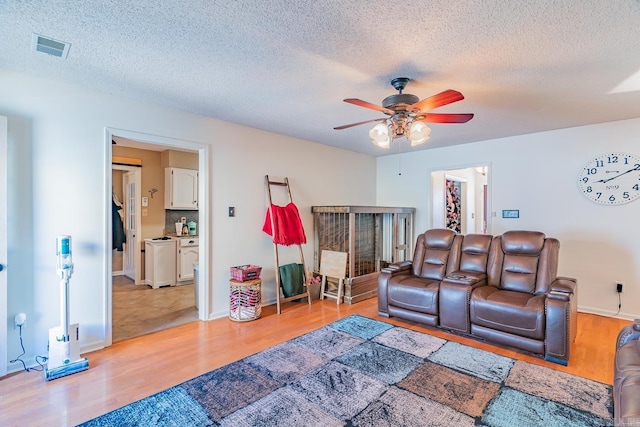 living room featuring visible vents, ceiling fan, a textured ceiling, and light wood finished floors