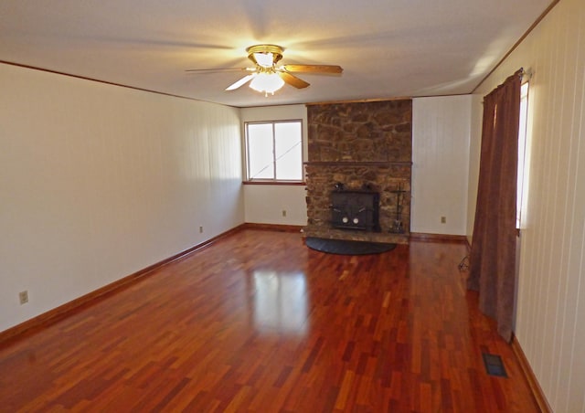 unfurnished living room featuring a stone fireplace, wood finished floors, visible vents, and a ceiling fan