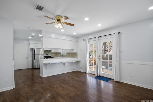 kitchen with light countertops, freestanding refrigerator, white cabinets, a peninsula, and under cabinet range hood