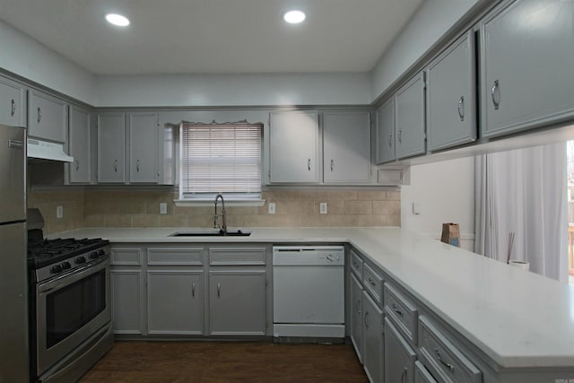 kitchen featuring under cabinet range hood, stainless steel appliances, a peninsula, a sink, and light countertops