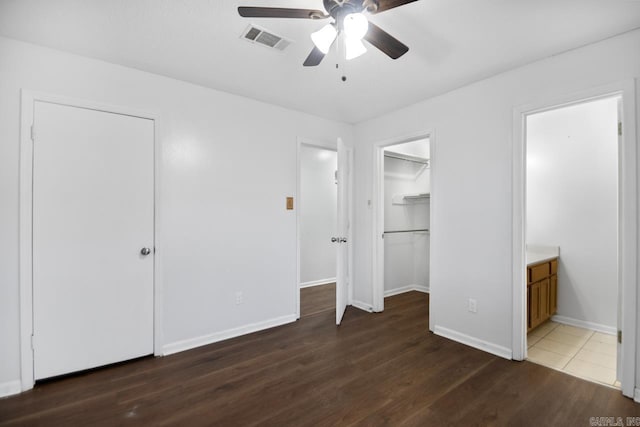 unfurnished bedroom featuring dark wood finished floors, visible vents, a spacious closet, ensuite bath, and baseboards