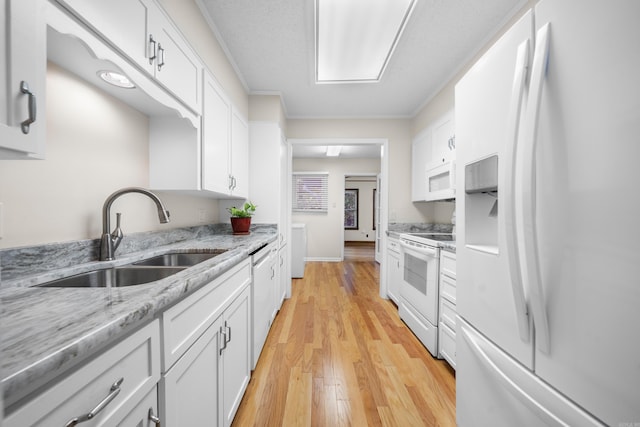 kitchen featuring white appliances, light stone counters, white cabinets, and a sink