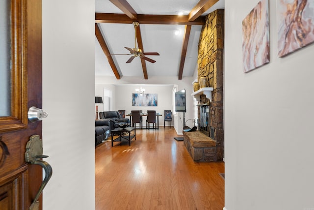 foyer featuring vaulted ceiling with beams, a stone fireplace, light wood finished floors, and ceiling fan with notable chandelier