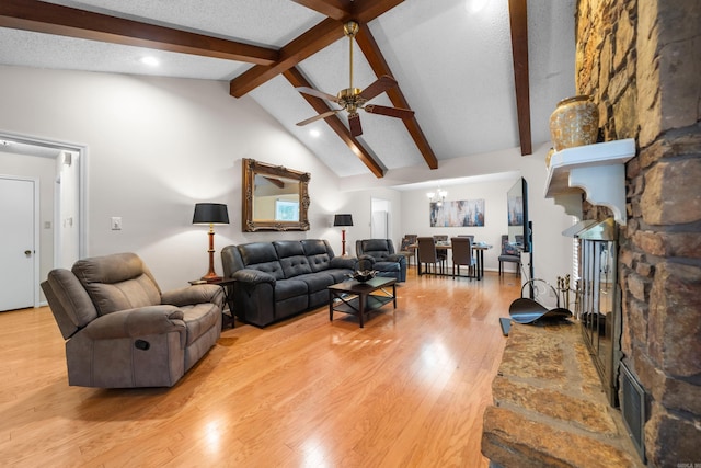 living room with wood finished floors, a textured ceiling, a stone fireplace, high vaulted ceiling, and beam ceiling