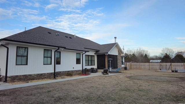 rear view of house featuring roof with shingles, a patio area, a fenced backyard, and a lawn