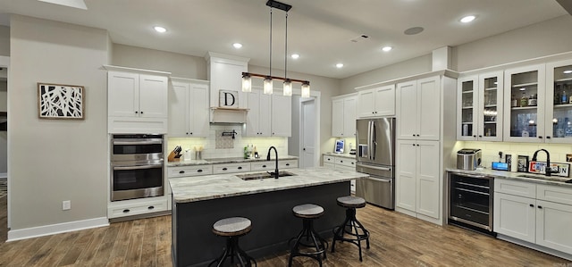 kitchen with wine cooler, decorative light fixtures, stainless steel appliances, a sink, and an island with sink