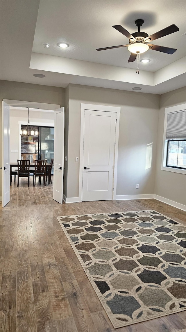 interior space featuring a tray ceiling, recessed lighting, wood finished floors, baseboards, and ceiling fan with notable chandelier