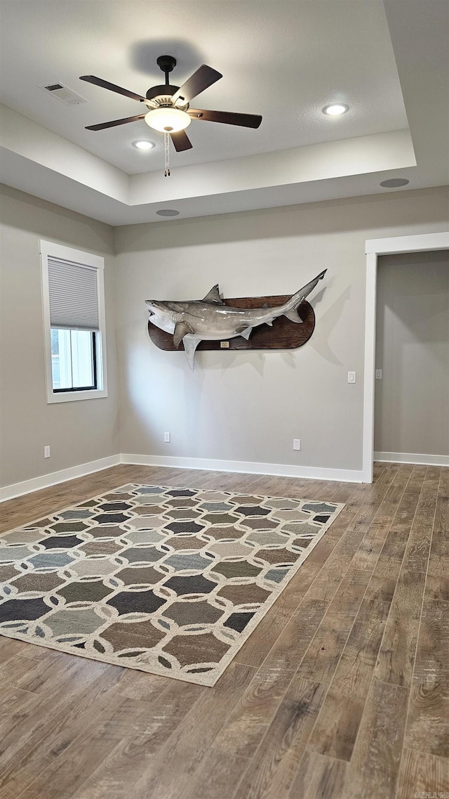 spare room with recessed lighting, a raised ceiling, visible vents, wood finished floors, and baseboards