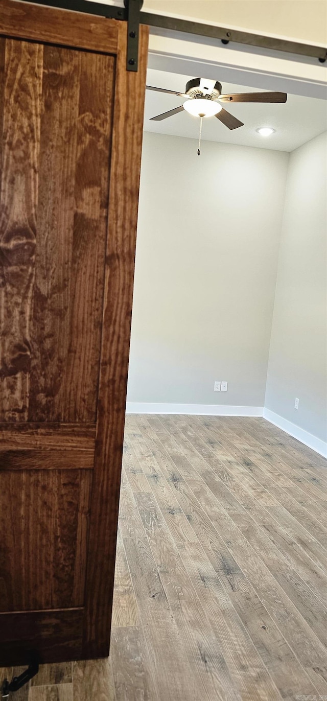 unfurnished room featuring a ceiling fan, wood finished floors, baseboards, and a barn door