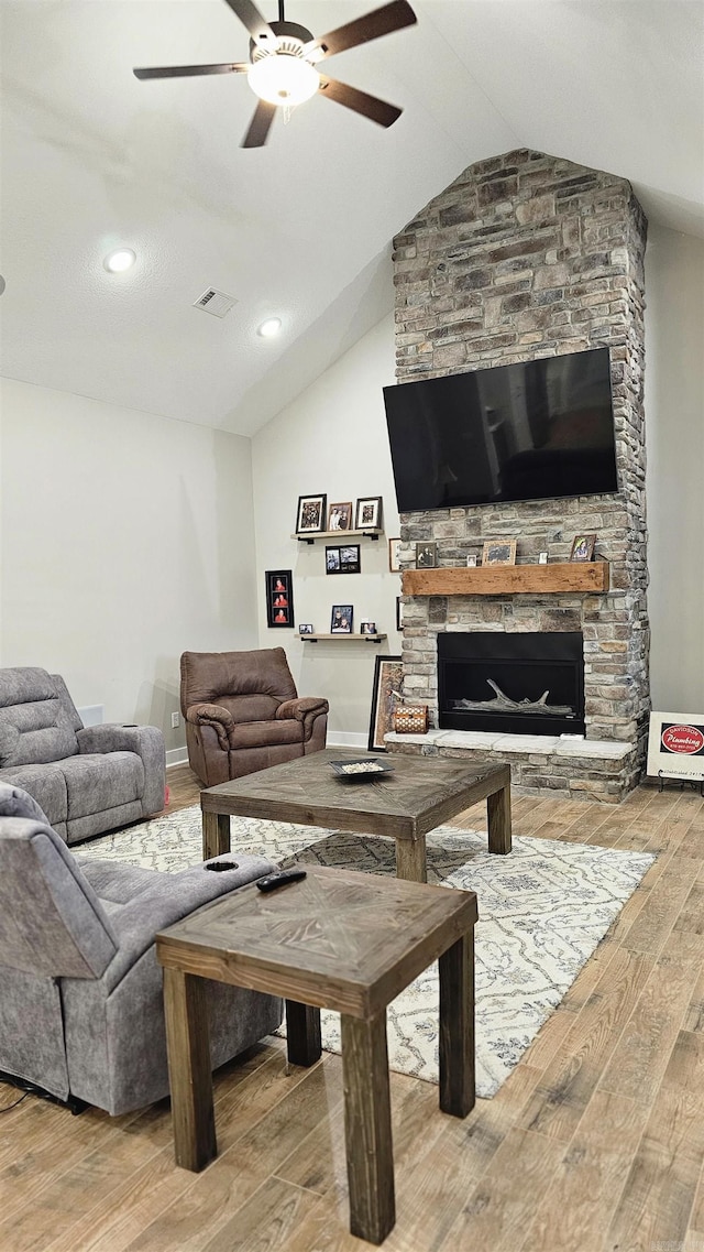 living area featuring lofted ceiling, visible vents, ceiling fan, a stone fireplace, and wood finished floors