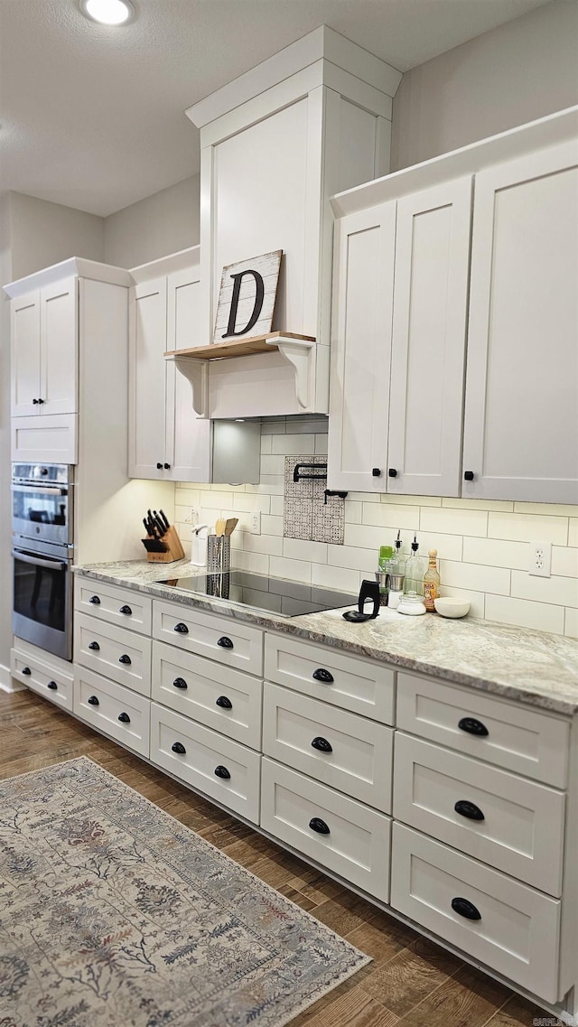 kitchen with double oven, black electric stovetop, dark wood-type flooring, white cabinetry, and decorative backsplash