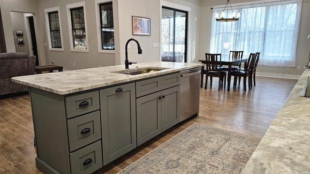 kitchen with decorative light fixtures, gray cabinetry, stainless steel dishwasher, a sink, and an island with sink