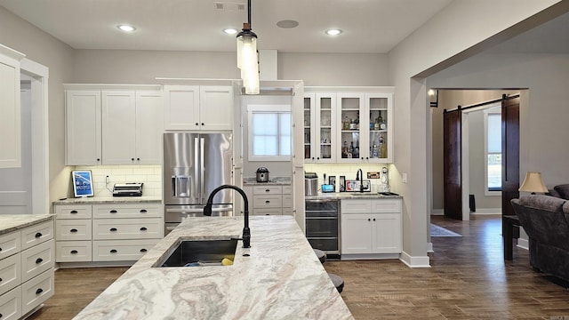 kitchen featuring a barn door, beverage cooler, glass insert cabinets, stainless steel refrigerator with ice dispenser, and a sink