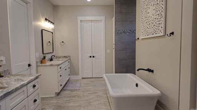 bathroom with a sink, two vanities, a freestanding tub, and baseboards