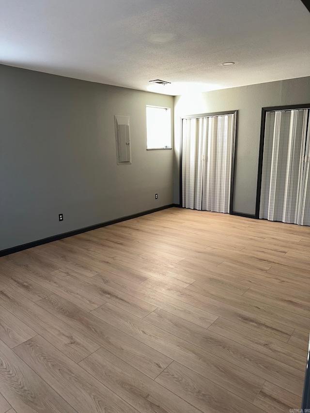 empty room featuring baseboards, light wood-type flooring, visible vents, and electric panel