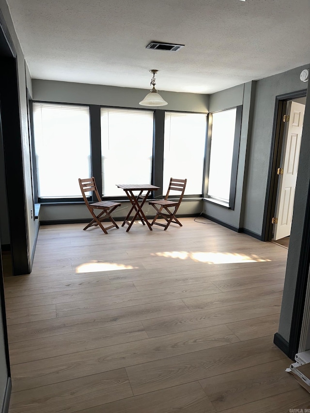 interior space featuring a textured ceiling, light wood-style flooring, visible vents, and baseboards