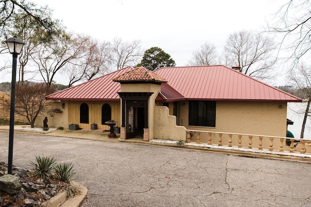 mediterranean / spanish home with a standing seam roof, metal roof, brick siding, and a chimney