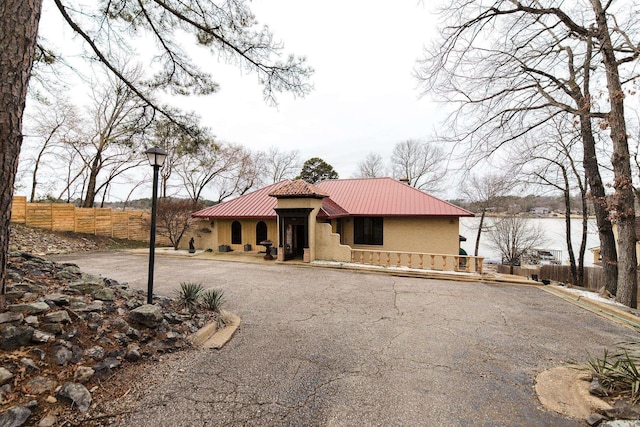 mediterranean / spanish-style home featuring metal roof, a water view, fence, and stucco siding