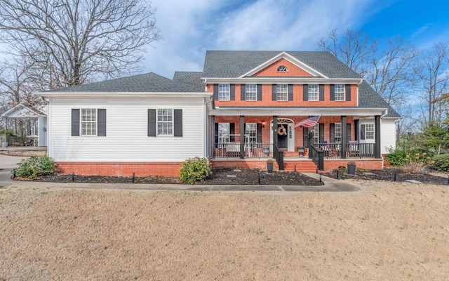 view of front of home featuring covered porch, roof with shingles, brick siding, and a front yard