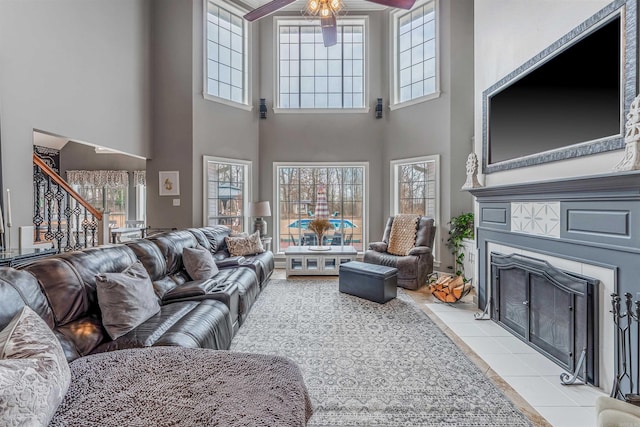 living area featuring ceiling fan, stairs, a tiled fireplace, and light tile patterned flooring