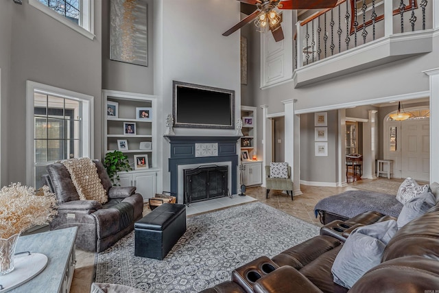 living room with a towering ceiling, a fireplace with flush hearth, built in shelves, and baseboards