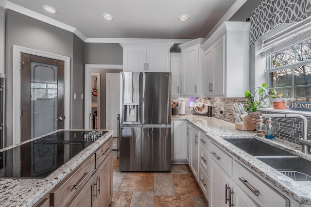 kitchen featuring white cabinets, light stone counters, black electric cooktop, stainless steel refrigerator with ice dispenser, and a sink