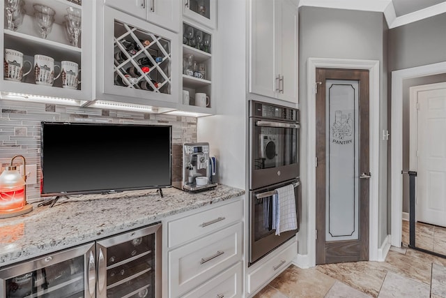 kitchen with tasteful backsplash, beverage cooler, white cabinets, light stone countertops, and stainless steel double oven