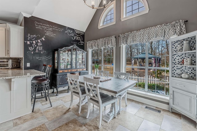 interior space featuring high vaulted ceiling, a toaster, visible vents, stone tile flooring, and an inviting chandelier