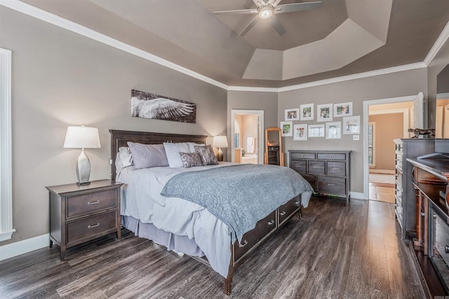 bedroom featuring baseboards, dark wood finished floors, ensuite bath, ornamental molding, and a tray ceiling