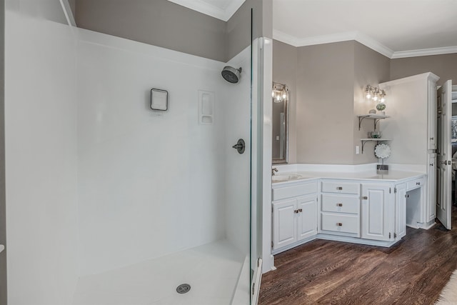 full bath with double vanity, ornamental molding, wood finished floors, a walk in shower, and a sink