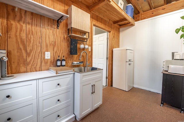 kitchen with light countertops, wood walls, white cabinetry, open shelves, and a sink