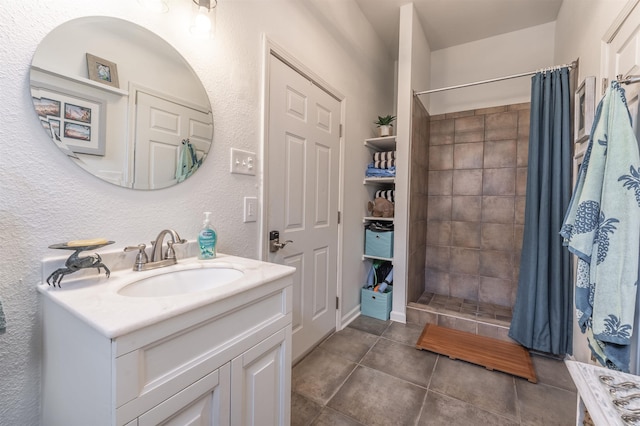 full bathroom featuring tile patterned flooring, a textured wall, a shower stall, and vanity