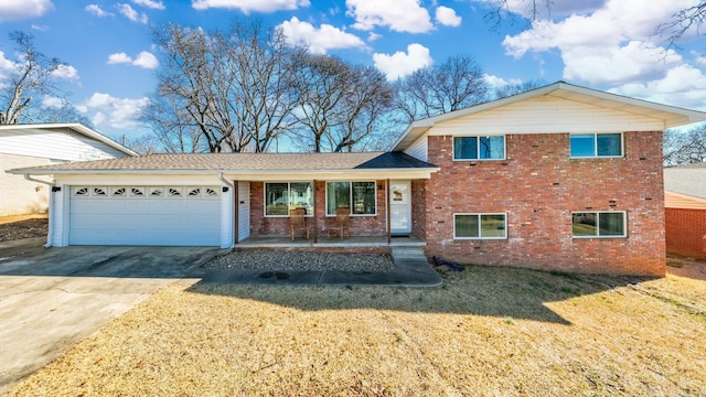 split level home featuring a porch, an attached garage, brick siding, driveway, and a front lawn