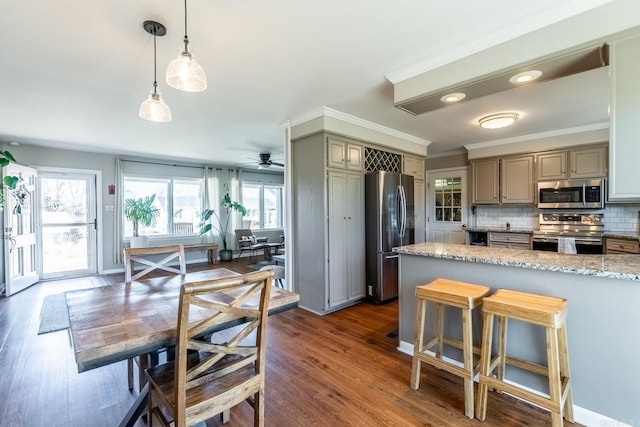 kitchen with gray cabinetry, stainless steel appliances, hanging light fixtures, tasteful backsplash, and dark wood finished floors