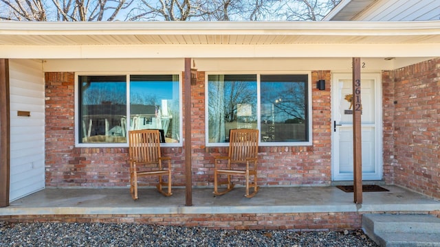 doorway to property featuring covered porch and brick siding