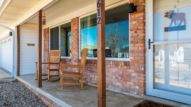 view of exterior entry with a porch, brick siding, and a garage