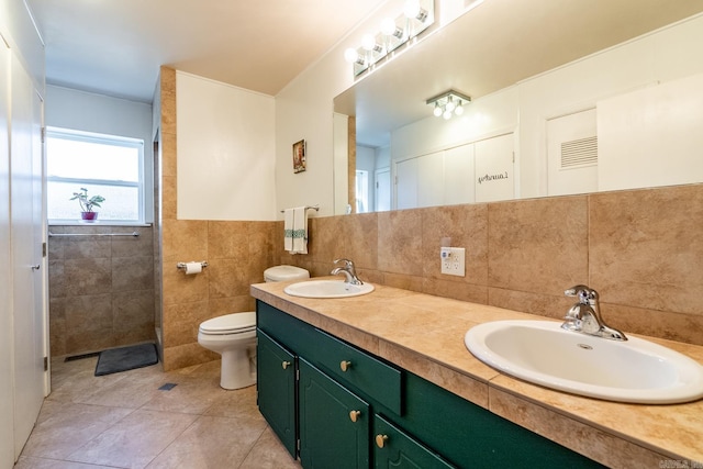 bathroom featuring toilet, double vanity, a sink, and tile walls