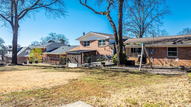 back of property with a yard, fence, a sunroom, and brick siding