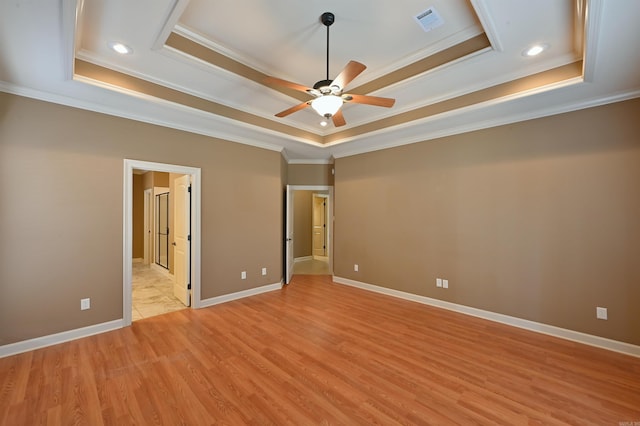 unfurnished bedroom featuring visible vents, baseboards, light wood-style flooring, ornamental molding, and a tray ceiling