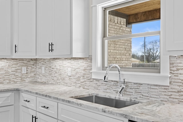 kitchen featuring light stone counters, white cabinetry, a sink, and tasteful backsplash