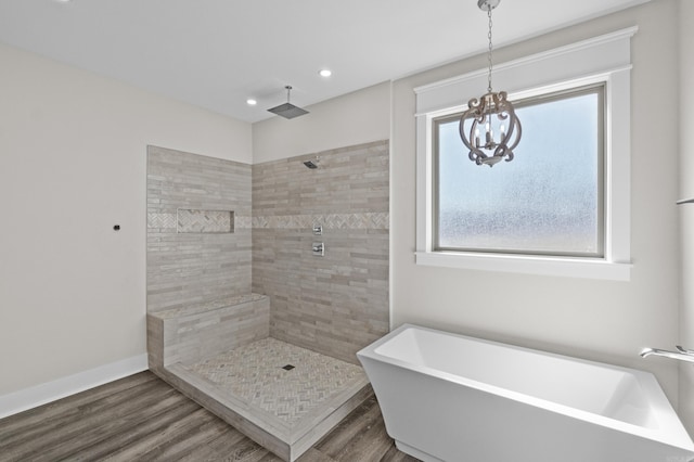 full bath featuring baseboards, wood finished floors, a tile shower, a freestanding bath, and a chandelier