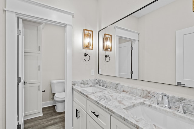 full bathroom with toilet, double vanity, a sink, and wood finished floors