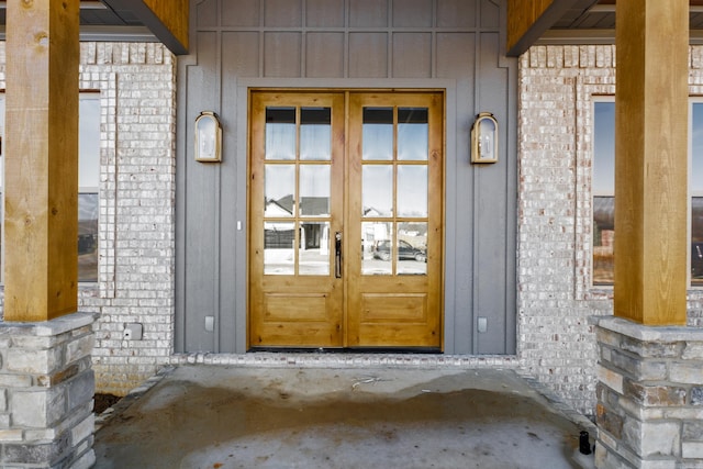 doorway to property with board and batten siding, french doors, and brick siding