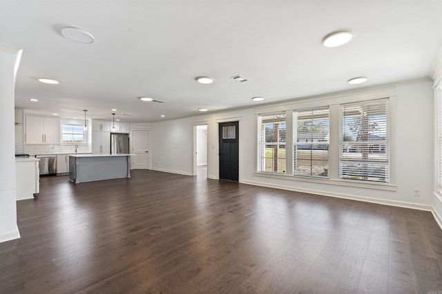 unfurnished living room featuring dark wood-type flooring, a healthy amount of sunlight, and baseboards