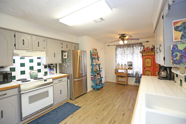 kitchen featuring white electric stove, tile countertops, freestanding refrigerator, light wood-type flooring, and under cabinet range hood