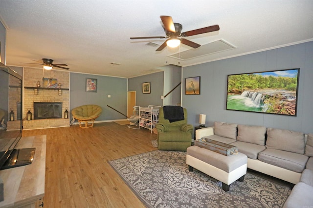 living room featuring wood finished floors, visible vents, ornamental molding, a brick fireplace, and attic access